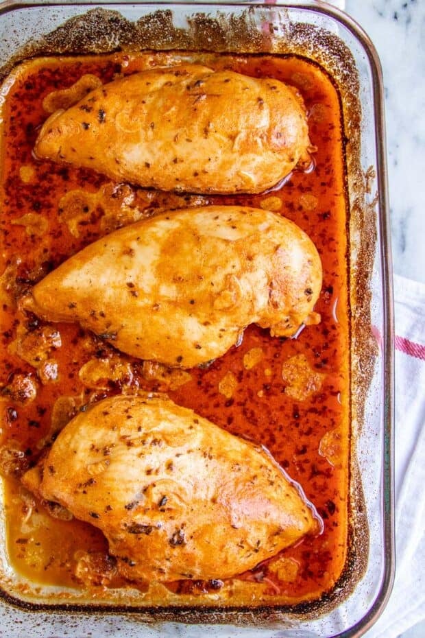 three chicken breasts in a glass cooking dish after being cooked in red marinade