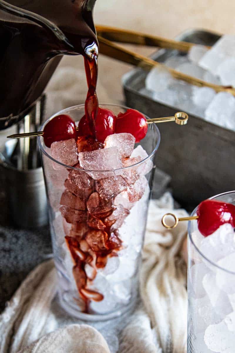 pouring cherry dr. pepper syrup into iced glass from pitcher
