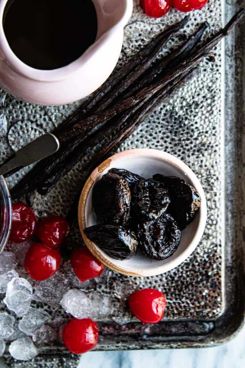 simple syrup, vanilla beans, prunes, and cherries all on silver board