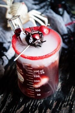 A dark cosmo cocktail with a test tube of pomegranate juice and a black widow spider garnish.