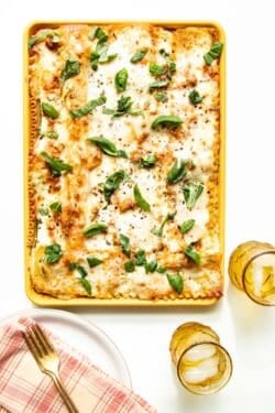 A table setting of plates and drinks with a sheet pan of freshly baked lasagna in the middle.