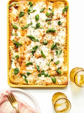 A table setting of plates and drinks with a sheet pan of freshly baked lasagna in the middle.