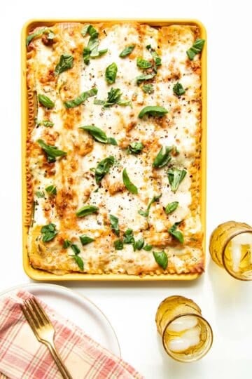 A table setting of plates and drinks with a sheet pan of freshly baked lasagna in the middle.