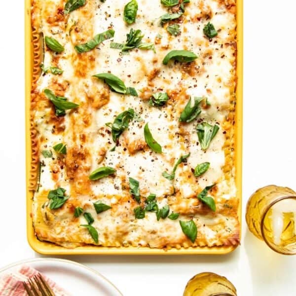 A table setting of plates and drinks with a sheet pan of freshly baked lasagna in the middle.